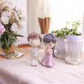 Go Hooked resin couple figurines in proposal pose, groom in white suit, bride in pink dress, for cake decor or home.