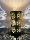 GoHooked dark brown metal table lamp with Ganesha cutouts, casting decorative shadows. Ideal for bedside or living room decor.