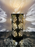 Go Hooked dark brown metal table lamp with Ganesha cutouts, casting decorative shadows. Ideal for bedrooms and living rooms.