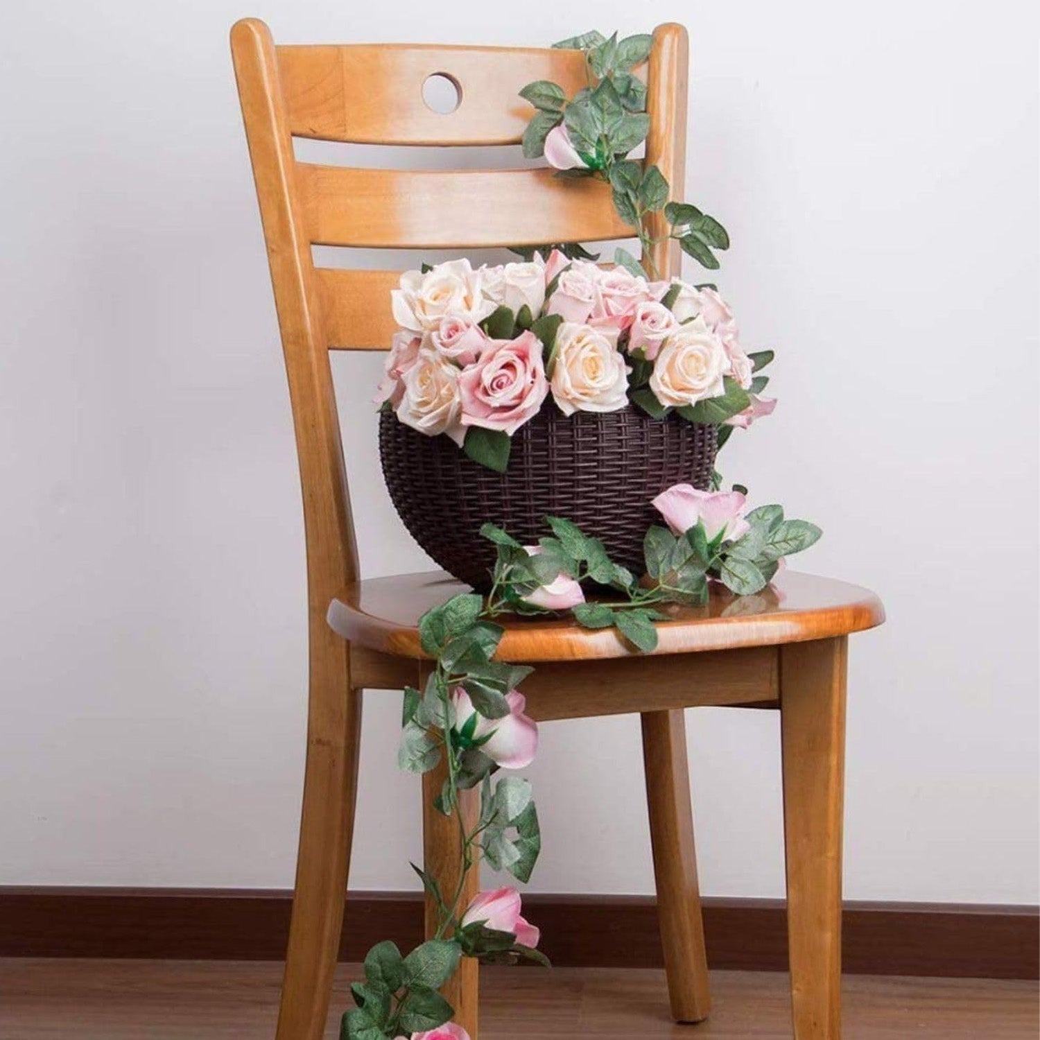 GoHooked dark brown plastic hanging pot filled with artificial pink roses and green vines sitting on a wooden chair.