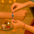 GoHooked designer rakhi with blue beads and a square metal charm tied on a man's wrist.