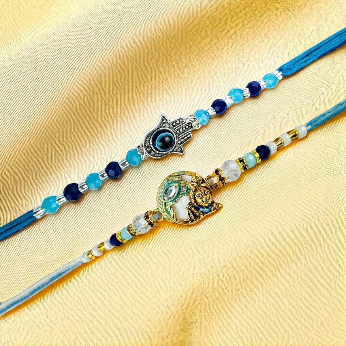 GoHooked designer rakhis with blue beads, Hamsa hand charm, and sun face charm on gold fabric.