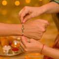 GoHooked multicolor designer rakhi with pearl beads and gold charm tied on a man's wrist by a woman.