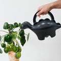 GoHooked black dinosaur-shaped plastic watering can with a 1-liter capacity, watering a houseplant.