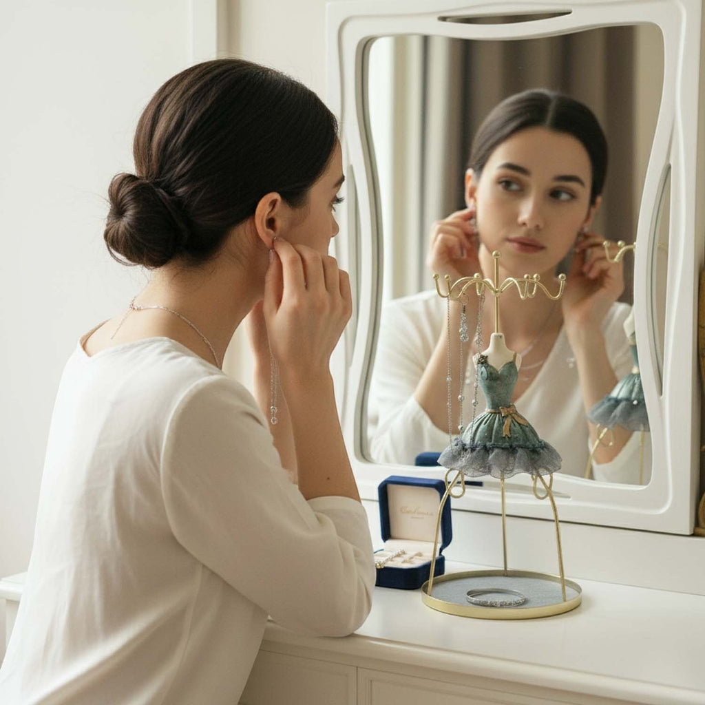 GoHooked grey doll dress jewelry holder stand on a vanity table with a woman putting on earrings in the mirror reflection