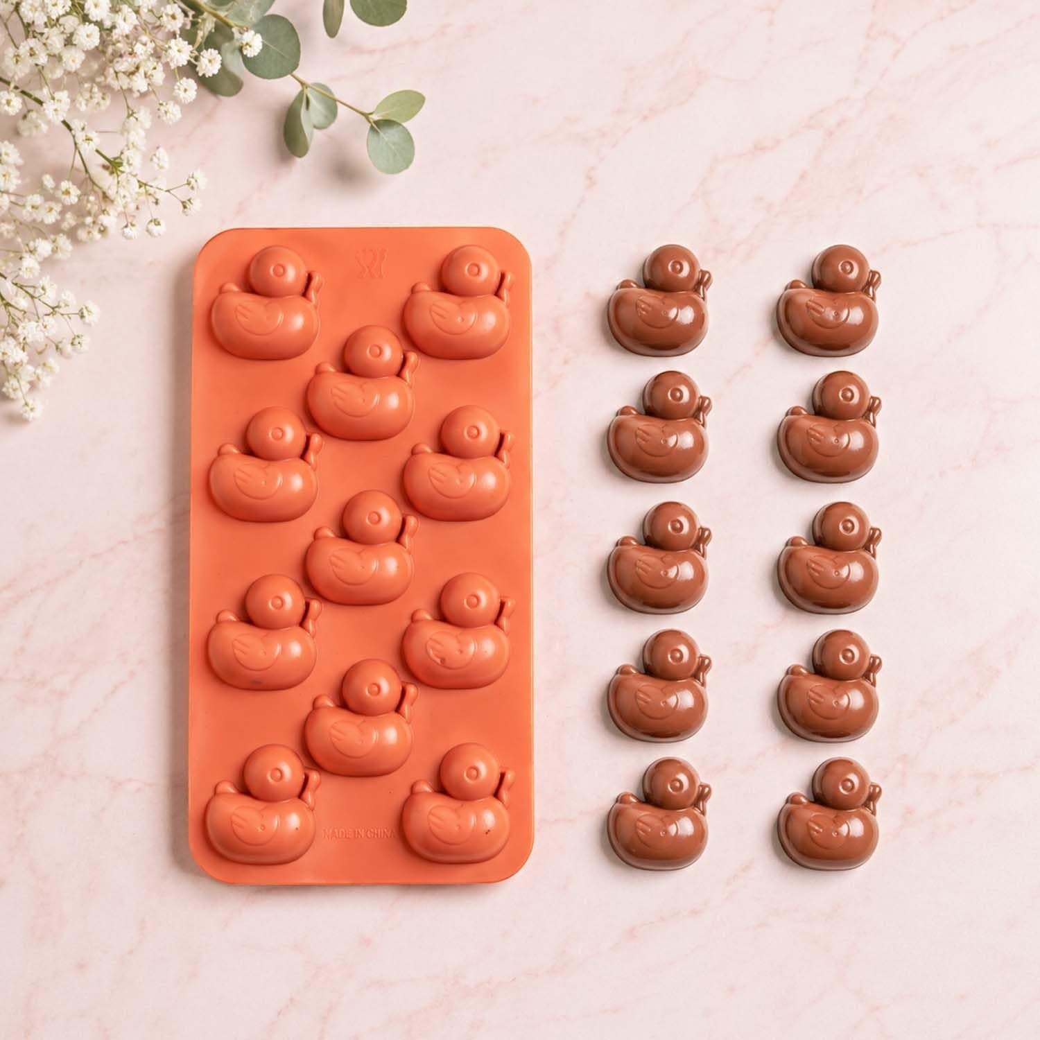 GoHooked silicone chocolate mold with 10 duck-shaped cavities and finished chocolate duck candies on a pink surface