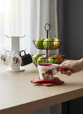 Go Hooked white ceramic coffee cup with red trim and floral design, held by a hand.