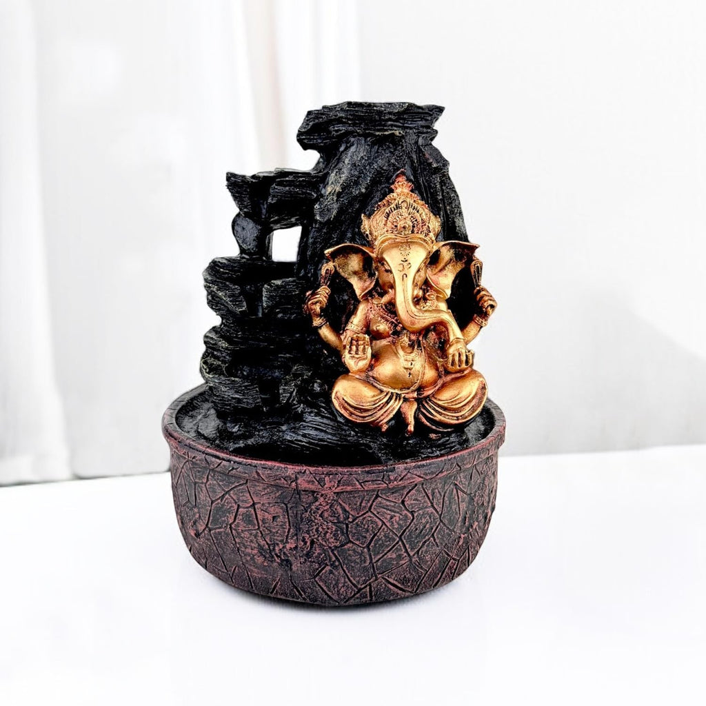 GoHooked gold Lord Ganesha sitting on a textured brown base with a black rock waterfall and LED lights. Polyresin.