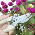 Go Hooked assorted gardening pruners with steel blades and beige ergonomic handles cutting pink flowers.