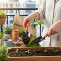 GoHooked gardening tools kit with orange handles, including a trowel and transplanter, used for planting seedlings in a wooden planter.
