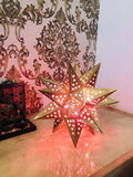 Go Hooked golden metal star-shaped table lamp with cut-out stars, casting a warm glow. Ideal for bedside or romantic decor.