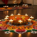 Go Hooked golden metal urli bowl with peacock motifs, filled with orange and yellow flowers, surrounded by tealights and marigold petals.