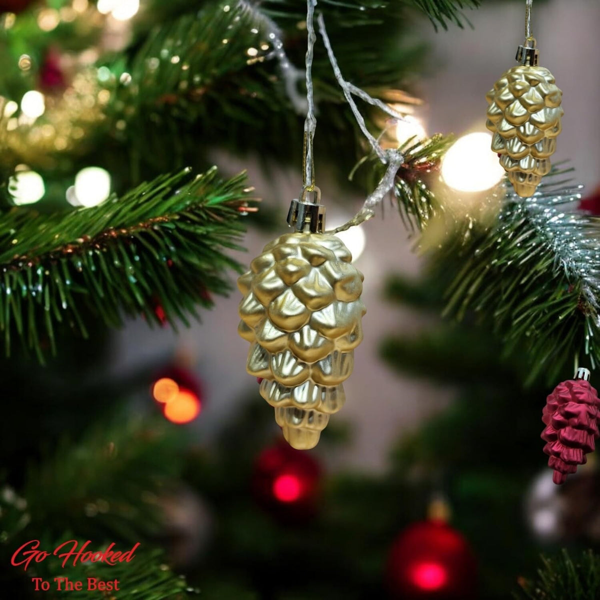 Go Hooked golden pine cone Christmas ornaments hanging on a tree with festive lights.