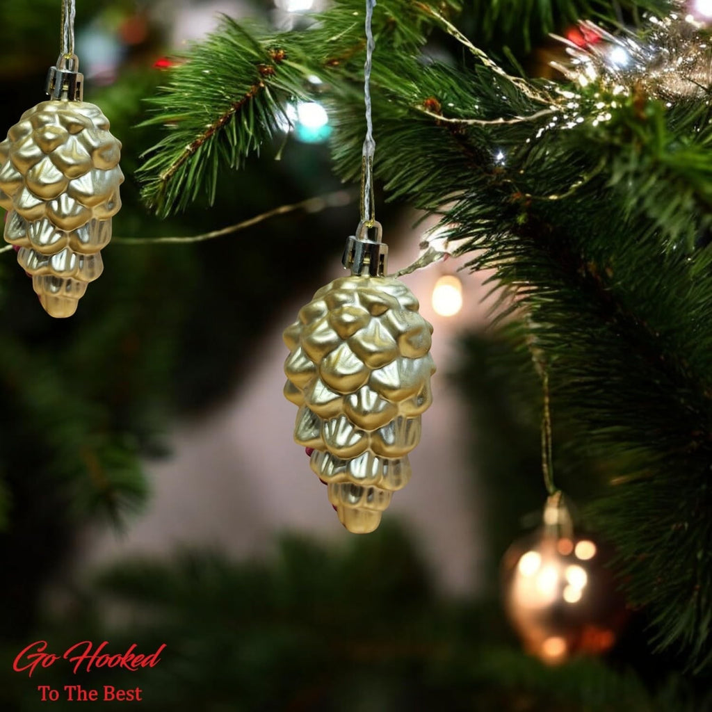 Go Hooked golden pine cone Christmas ornaments hanging on a tree with festive lights.