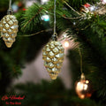 Go Hooked golden pine cone Christmas ornaments hanging on a tree with festive lights.