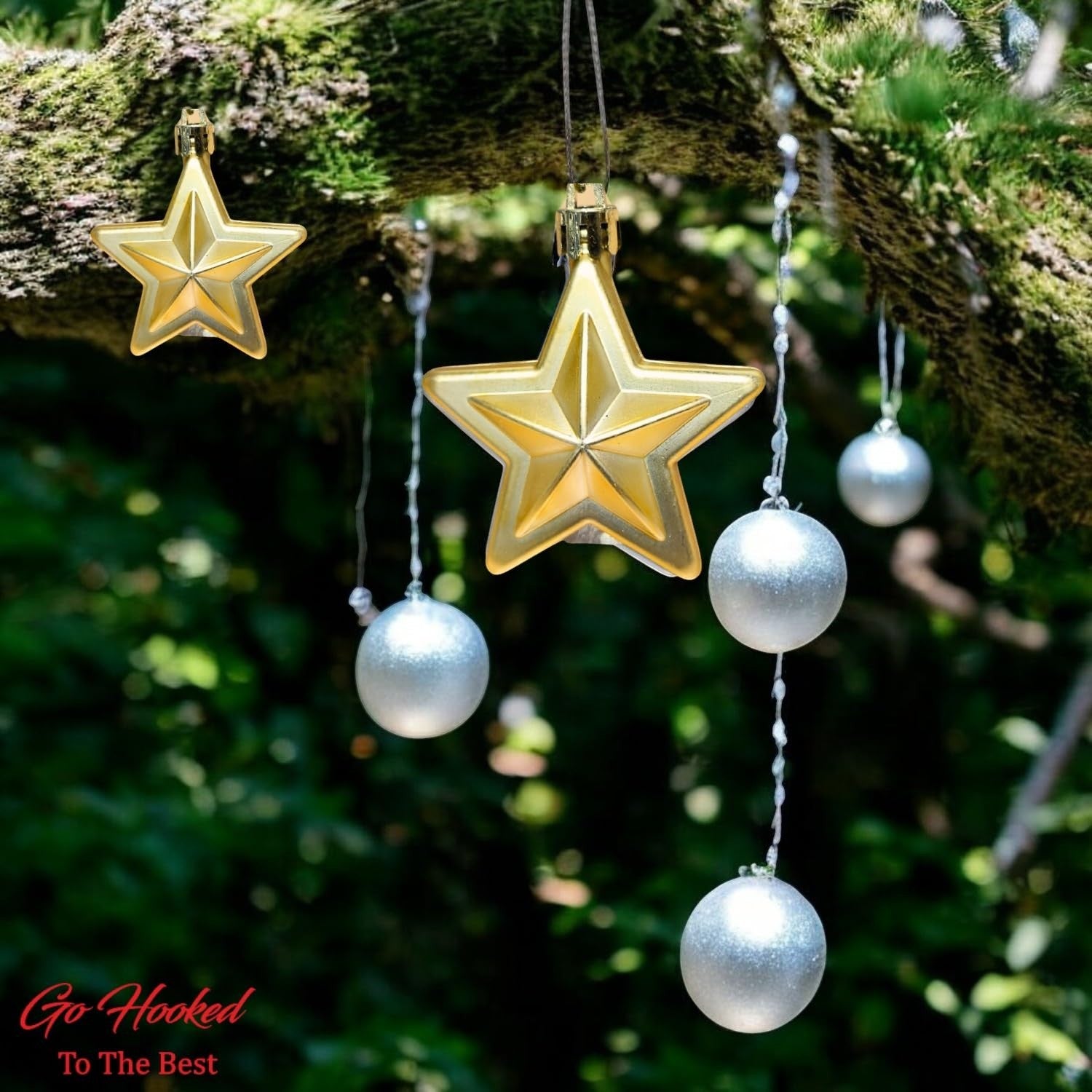 Go Hooked golden star and silver ball Christmas ornaments hanging on a mossy tree branch.