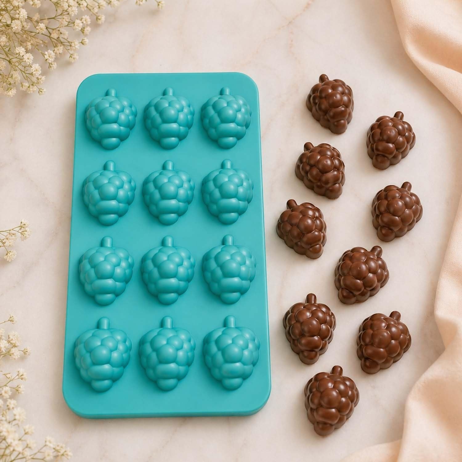 GoHooked teal silicone mold with 12 grape-shaped cavities next to finished chocolate grape candies on a marble surface