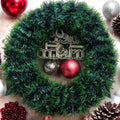GoHooked green tinsel Christmas wreath with "Merry Christmas" sign, red and silver baubles, pinecones, and berries.