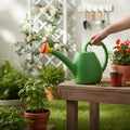 GoHooked green plastic watering can with yellow and red sprayer watering plants in a garden setting.