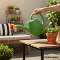 GoHooked green plastic watering can with yellow and red sprayer watering plants on a table