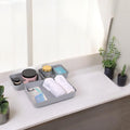 Go Hooked set of 3 grey plastic storage trays holding toiletries, towels, and razors on a countertop.