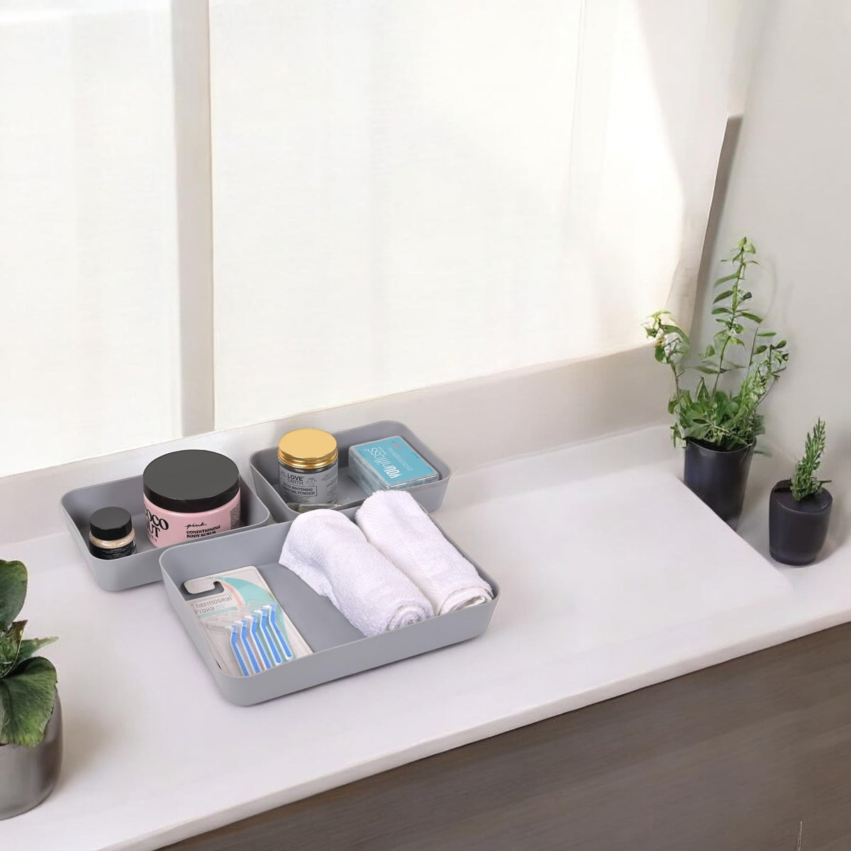 Go Hooked set of 3 grey plastic storage trays holding toiletries, towels, and razors on a countertop.