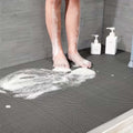 Go Hooked grey rubber anti-skid bathroom mat with honeycomb drainage pattern. Feet with soap suds.