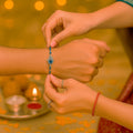 GoHooked blue beaded rakhi with Hamsa hand charm and evil eye detail being tied on a man's wrist.