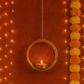 GoHooked matte gold metal hanging tealight holder with floral cut design and chain, lit candle inside.