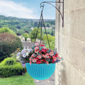 GoHooked light blue plastic hanging pot with woven texture, filled with colorful flowers, attached to a wall bracket.