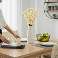 GoHooked light yellow artificial flowers in a white textured vase on a dining table.