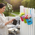 GoHooked metal hanging planters in pink, lime green, and blue, filled with colorful flowers, attached to a white fence.