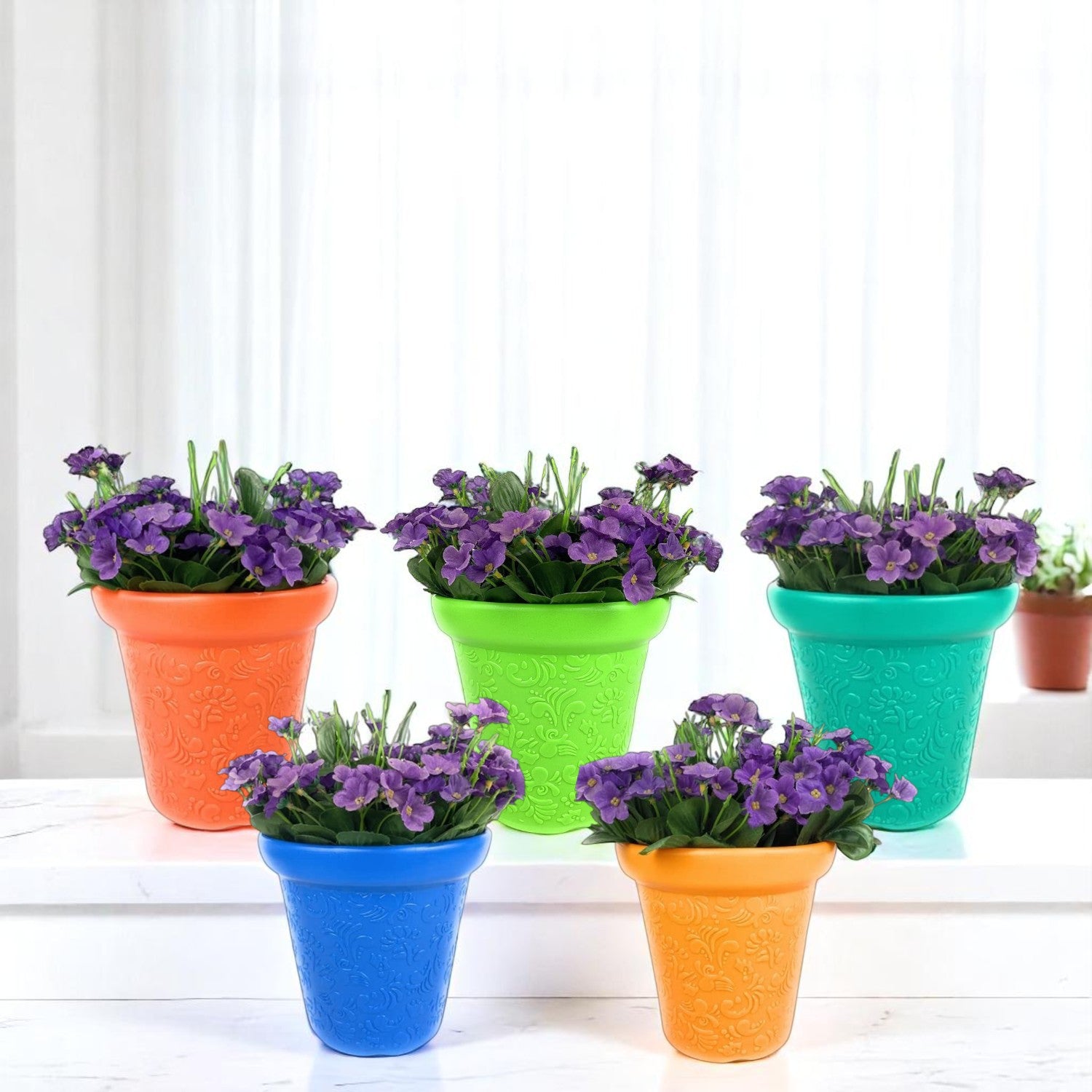 GoHooked set of five colorful plastic planter pots with embossed floral patterns and purple flowers on a white table