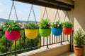 GoHooked multicolor round woven plastic hanging planters with plants on a balcony railing.