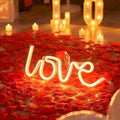 GoHooked white neon "love" sign surrounded by red artificial rose petals and LED candles.