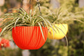GoHooked orange plastic hanging planter with woven texture and a spider plant. Yellow planter in background.