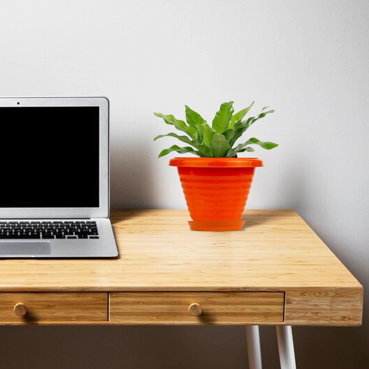 GoHooked orange plastic planter pot with saucer tray, featuring a modern ribbed design, holding a green plant on a wooden desk next to a laptop.