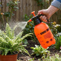 GoHooked orange plastic pressure sprayer watering a fern plant in a garden.