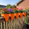Go Hooked orange plastic railing planters with colorful flowers on a wooden deck railing.