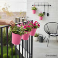 Go Hooked pink metal hanging planters with pink flowers on a balcony railing.