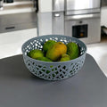 GoHooked light grey plastic fruit bowl with decorative cutouts, holding green and yellow fruit.