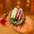 GoHooked Rakhi set with roli and chawal in glass vials, nestled in a decorative gold and green holder on a hand.