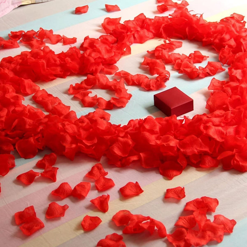 GoHooked 500 red artificial rose petals scattered on a striped surface with a small red gift box.