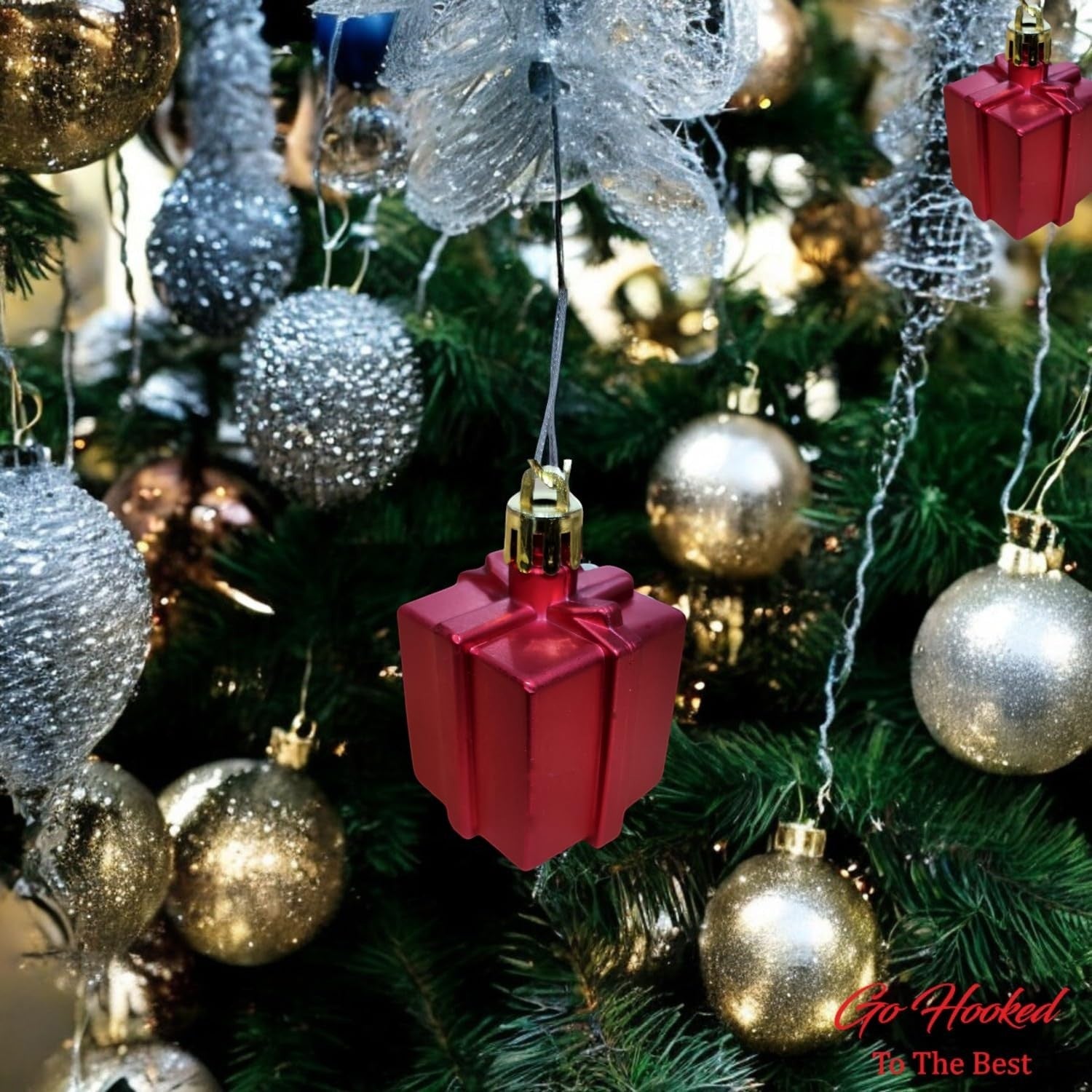 Go Hooked red glitter gift box Christmas ornament hanging on a decorated tree with gold and silver baubles.