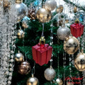 GoHooked red gift box Christmas ornaments with gold caps, hanging on a decorated tree with silver and gold baubles.