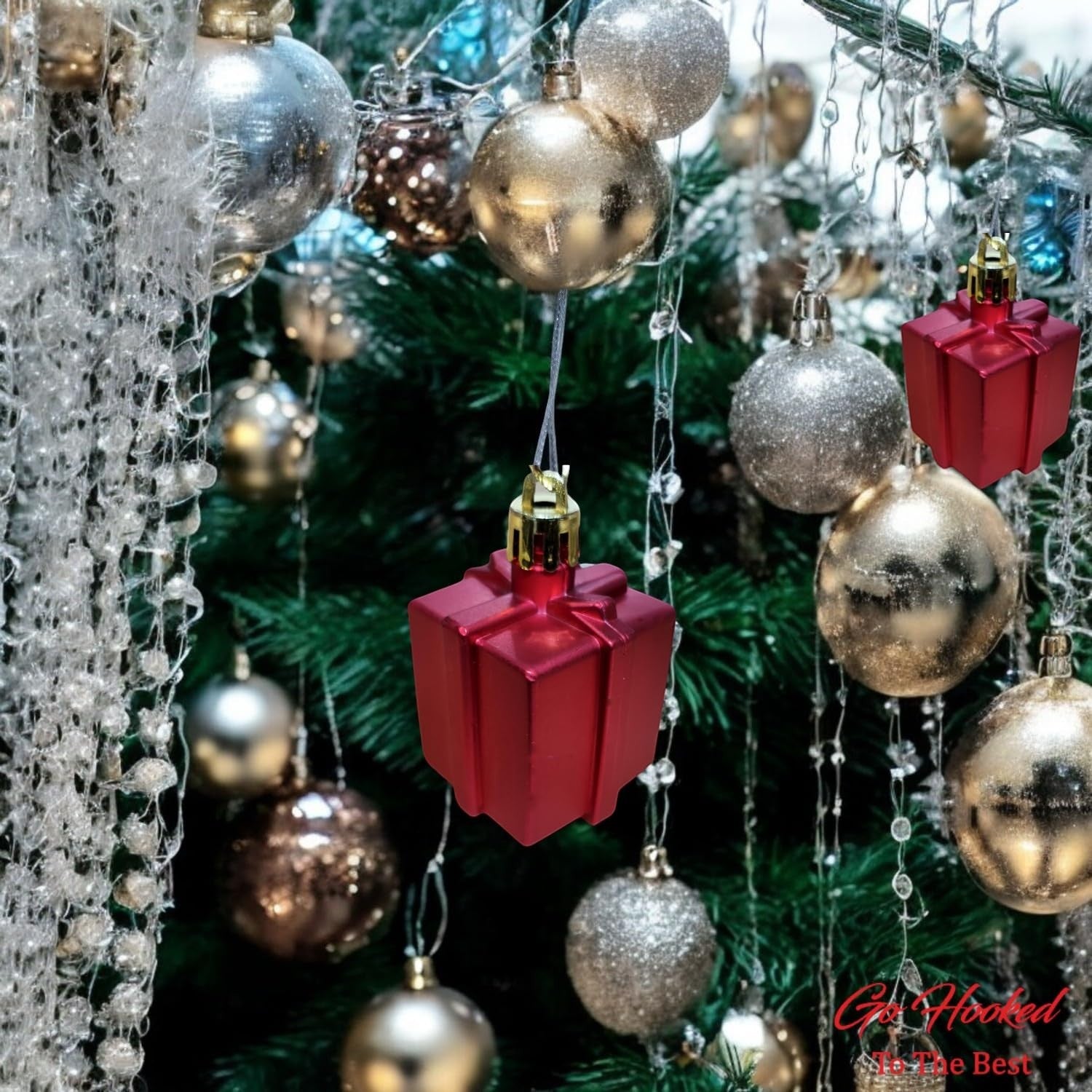GoHooked red gift box Christmas ornaments with gold caps, hanging on a decorated tree with silver and gold baubles.