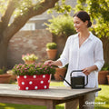 Go Hooked 12-inch red metal oval planter with white polka dots, holding pink flowers. Woman watering.
