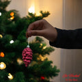 GoHooked red pine cone Christmas ornament with glitter details, held by a hand against a decorated tree.