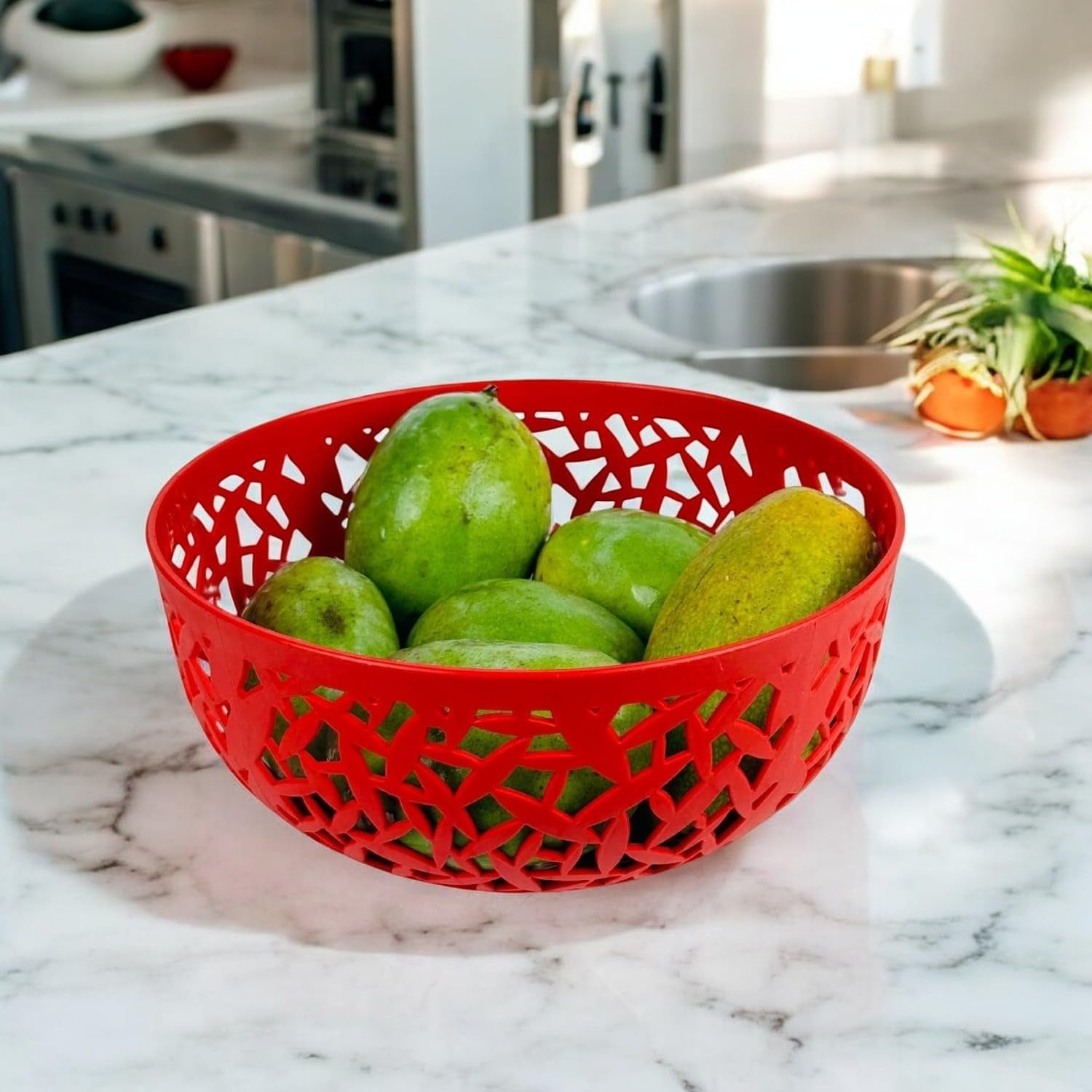 Go Hooked red plastic fruit bowl with intricate cutout design, filled with green fruits on a marble countertop.