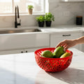 Go Hooked red plastic fruit bowl with intricate cutout design, holding green fruit on a marble countertop.